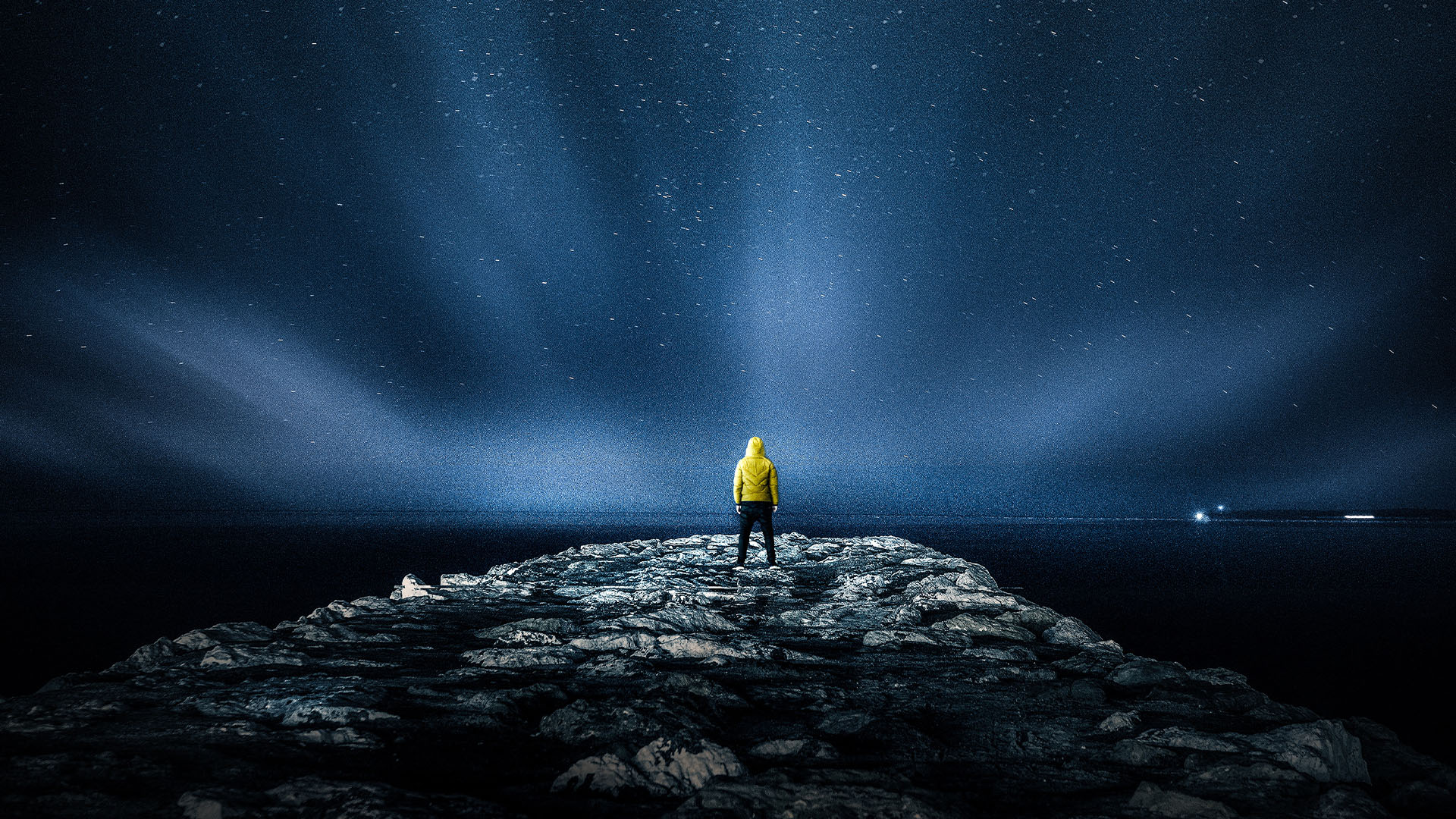 A figure in a yellow jacket looking out beneath a star-filled night sky