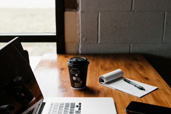Laptop, coffee and handwritten notes on a wooden café table beside a window.